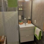 Bagno con box doccia in vetro, lavabo e asciugamani verdi