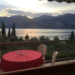 Balcone con tavolo rosso e sedie, vista lago al tramonto