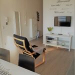 Soggiorno con poltrona, TV e scritta di benvenuto multilingue sulla parete